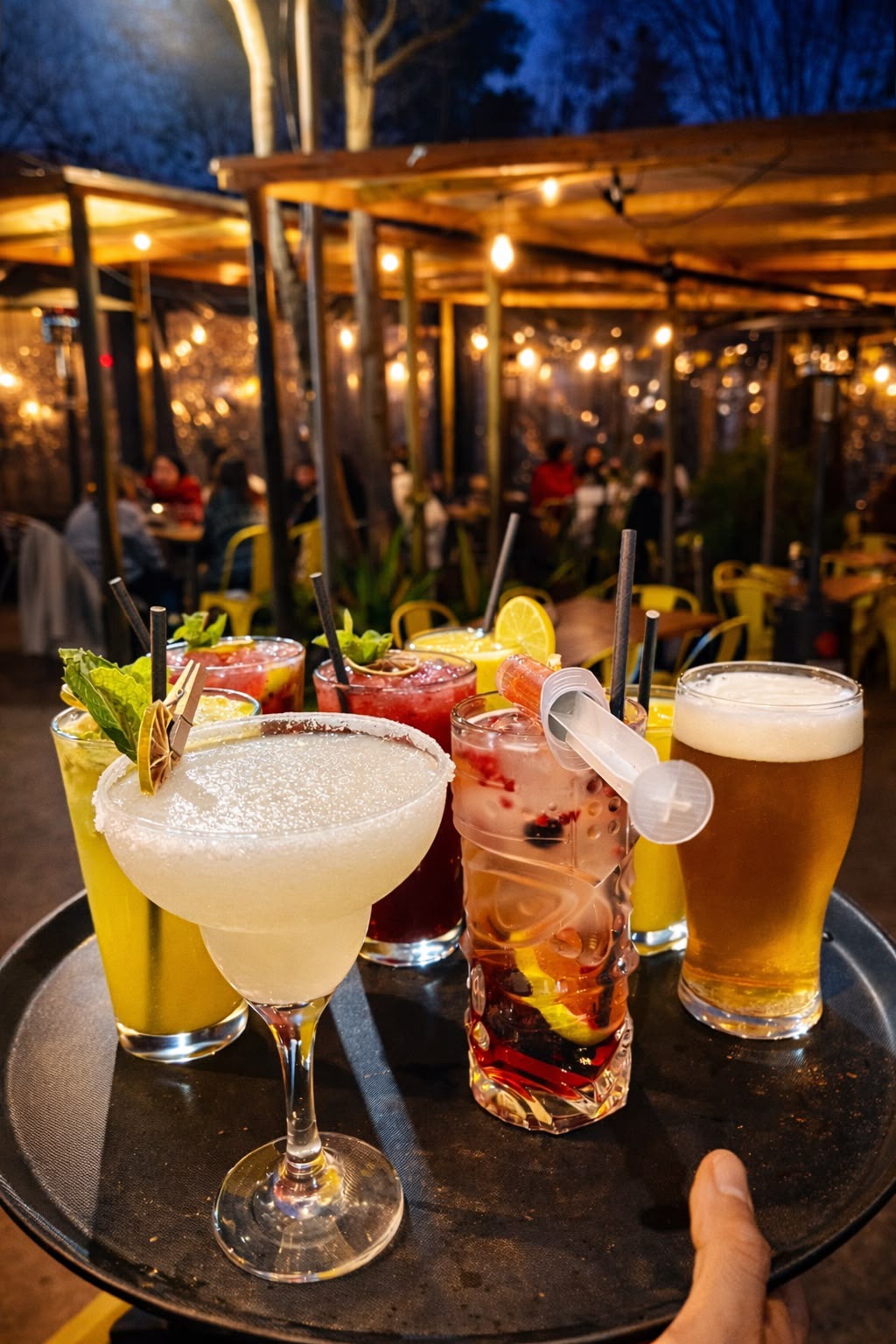 Bandeja de cócteles de Bravo's Restobar servida en la terraza al anochecer, con clientes de fondo