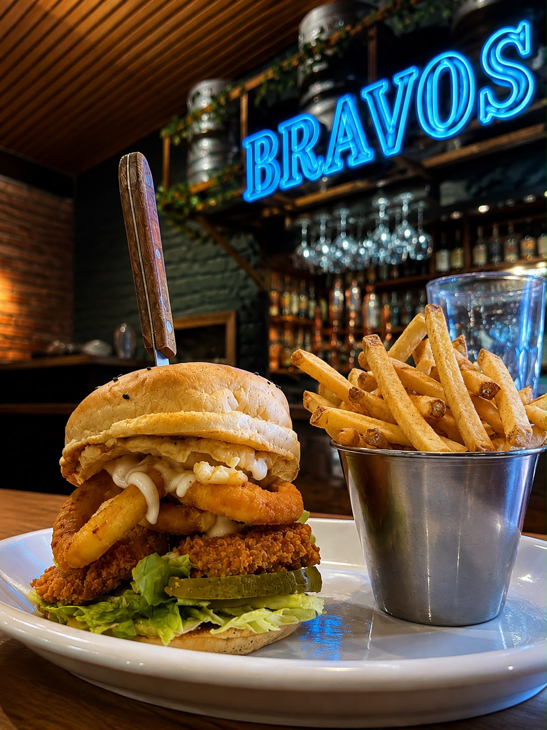 Hamburguesa crispy de Bravo's Restobar con papas fritas, bajo el letrero neón del local